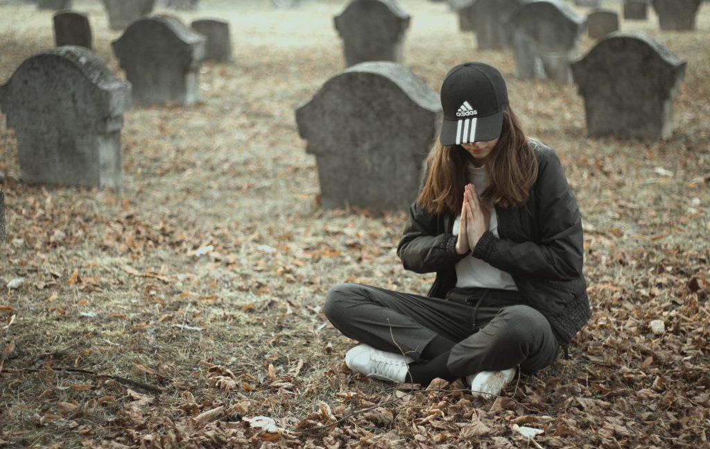 Sennik śmierć rodziców - dziewczyna modli się nad grobem rodzica, wyjaśniamy znaczenie snu o śmierci rodziców