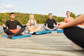 Grupa osób praktykująca jogę na pomoście nad jeziorem, co ilustruje warsztaty jogi na łonie natury