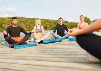 Grupa osób praktykująca jogę na pomoście nad jeziorem, co ilustruje warsztaty jogi na łonie natury