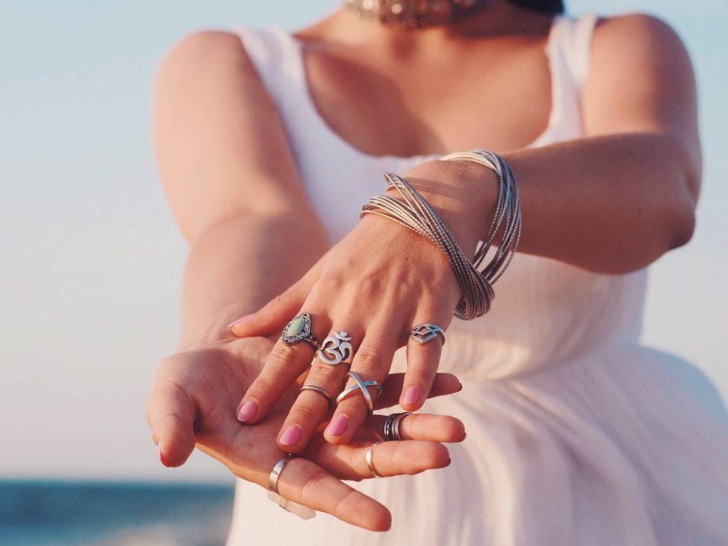 close up hands with boho gypsy silver accessories. Woman standing on the beach at summer near sea.