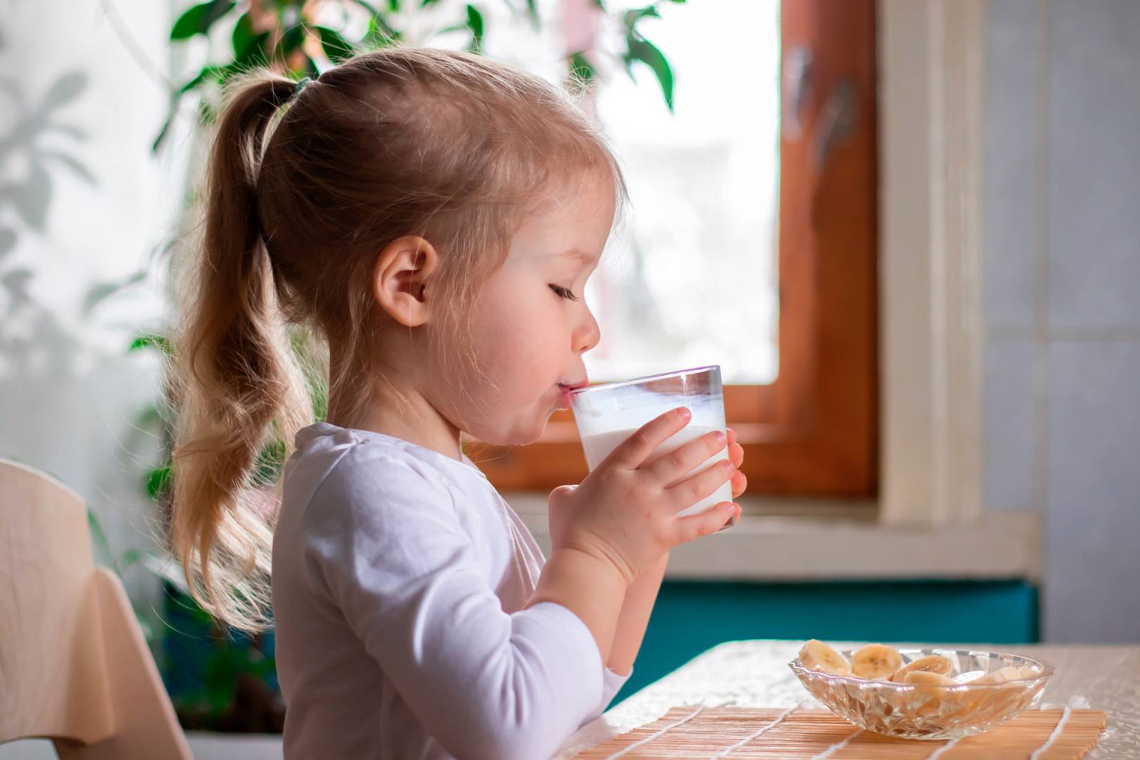 a little cheerful girl having breakfast with pieces of bananas a