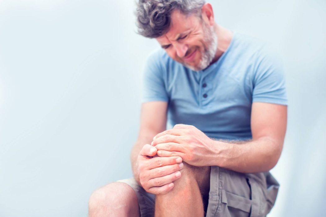 Closeup man hand holding knee with pain on bed, health care and