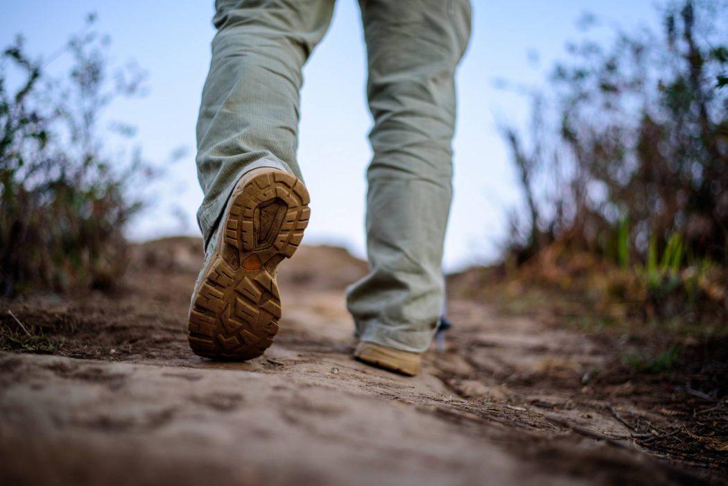 Close up feet Hiker man wearing boots to travel walking in a gre