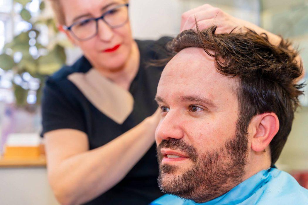 Man while hairdresser attaching a capillary prosthesis to his head