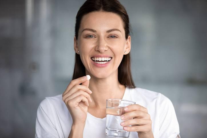 Cheerful woman holding pill glass of water looking at camera